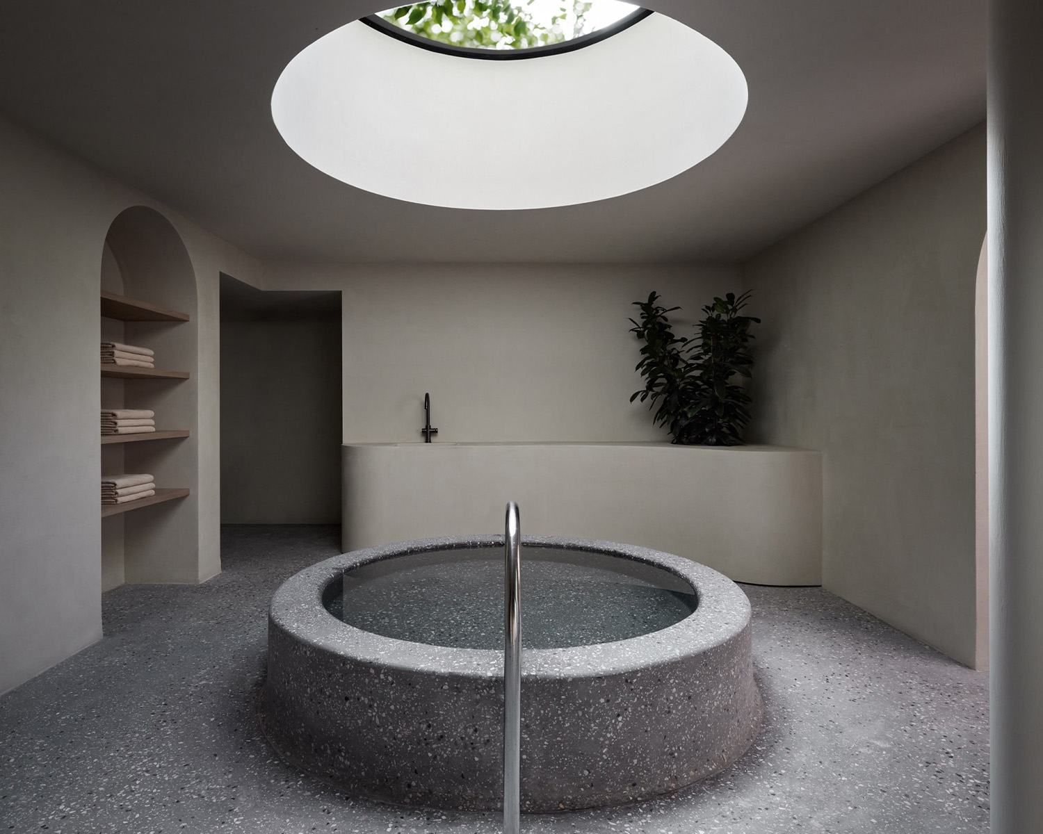 Spa area with a centrally located ice pool on a terrazzo floor. Above the pool light floods in through a big, round skylight.