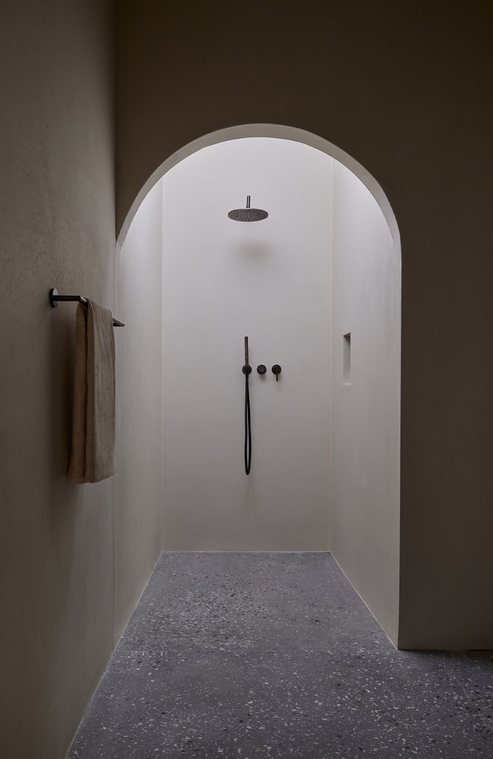 Shower with black fittings and plastered walls, terrazzo flooring.